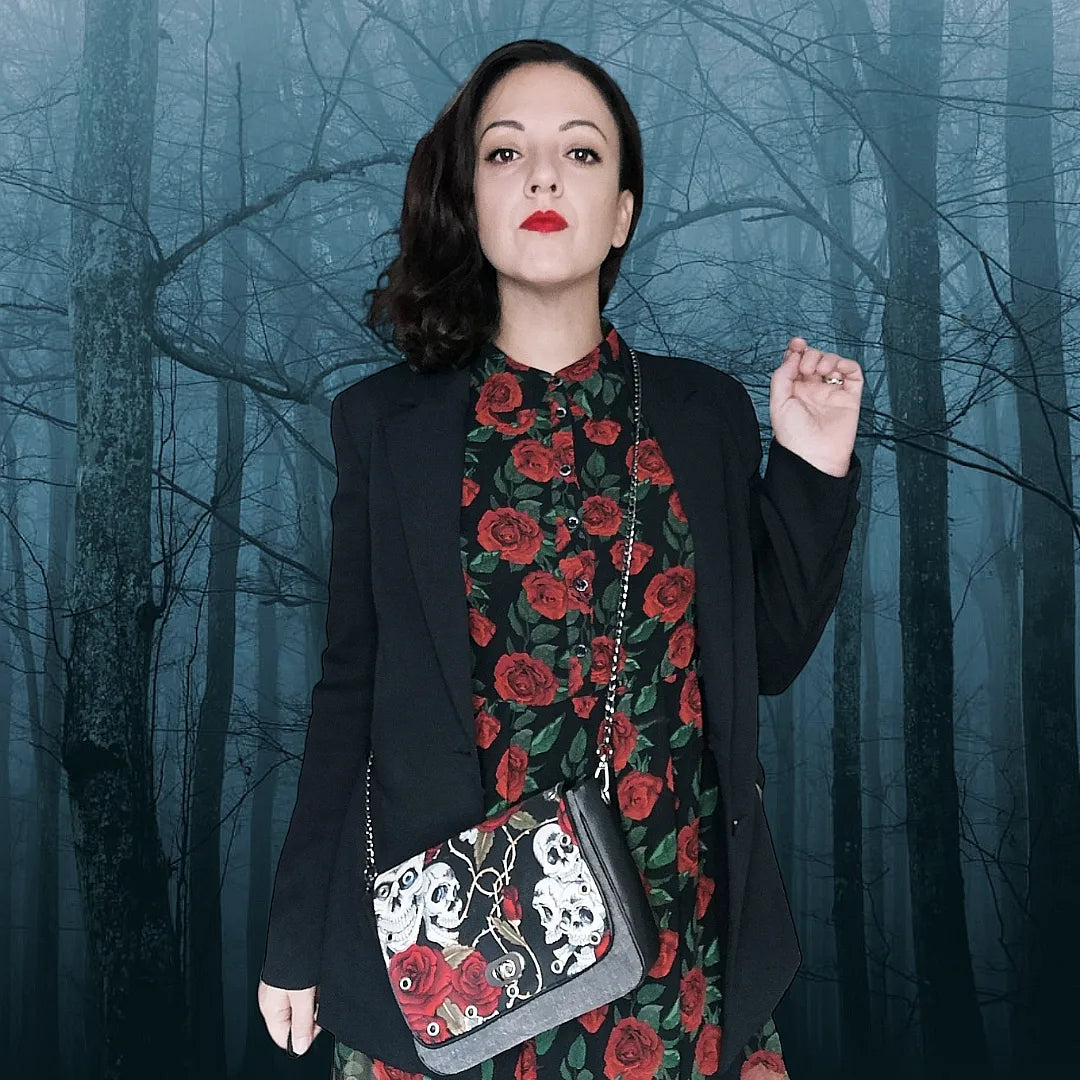 Sac à rabat motif têtes de mort et roses décoré d'œillets en métal argent. Muni d'un fermoir tourniquet argent et d'une chaîne canon de fusil bandouilère amovible.