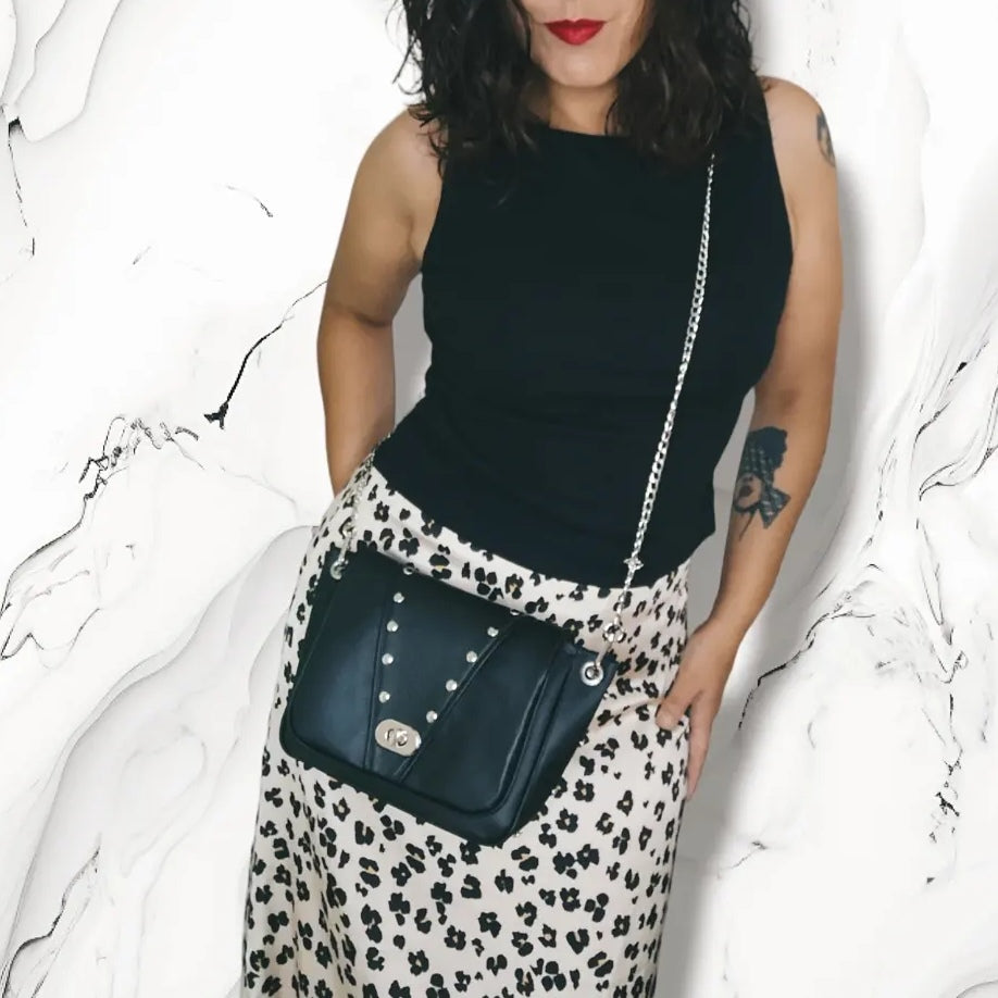 Sac à rabat en simili cuir noir, décoré de rivets en métal argent. Muni d'un fermoir tourniquet argent et d'une chaîne argent bandouilère amovible.