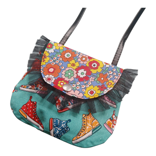 Petit sac bandoulière artisanal Bonnie pour enfant, motif baskets vintage et fleurs multicolores sur fond turquoise, avec volants en tulle noir sur les côtés.
